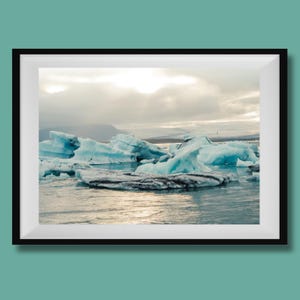May include: A framed print featuring a landscape of icebergs floating in a body of water. The icebergs are a vibrant blue, contrasting with the overcast sky. The water reflects the light, creating a serene scene.