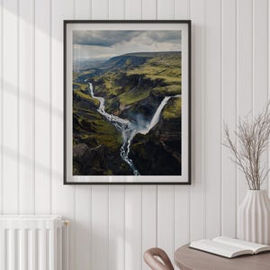 Pu&ograve; includere: Fotografia incorniciata di un paesaggio con una cascata e un fiume che attraversa un canyon verde. L'immagine &egrave; in una cornice nera e appesa a una parete bianca. Un vaso con rami secchi e una lampada da tavolo sono su un tavolo vicino.