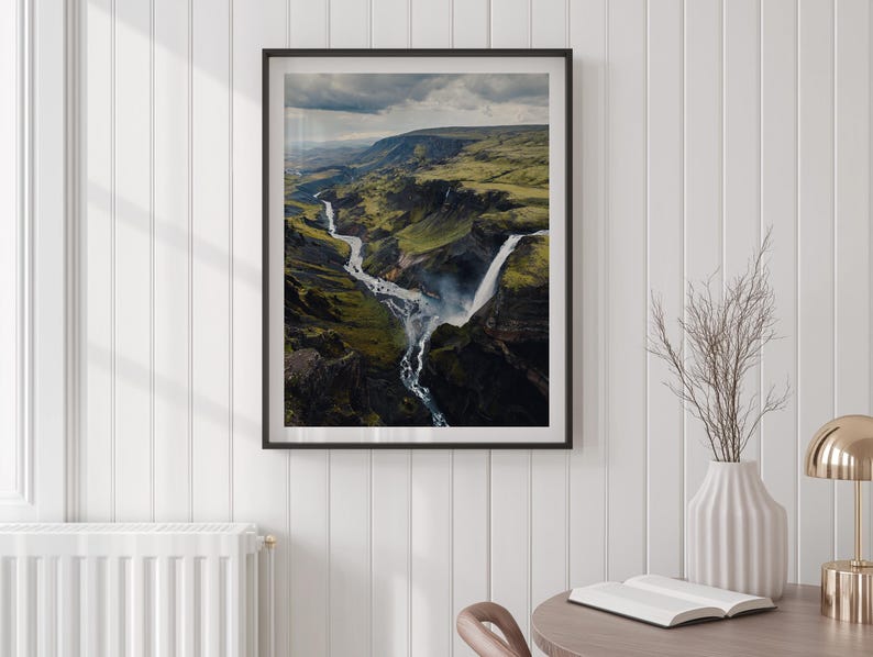 Pu&ograve; includere: Fotografia incorniciata di un paesaggio con una cascata e un fiume che attraversa un canyon verde. L'immagine &egrave; in una cornice nera e appesa a una parete bianca. Un vaso con rami secchi e una lampada da tavolo sono su un tavolo vicino.
