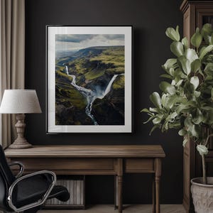 Pu&ograve; includere: Fotografia incorniciata di un paesaggio di cascata in una valle verde. L'opera d'arte &egrave; esposta su una parete scura sopra una scrivania in legno con una lampada e una sedia da ufficio nera. Una pianta in vaso &egrave; a destra.