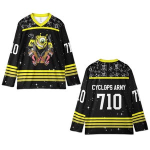 May include: Black hockey jersey with yellow accents and a V-neck collar. The front features a cartoon cyclops with a dog graphic. The jersey has the number 710 on the front and back, with the words "CYCLOPS ARMY" on the back.