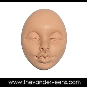 May include: A close-up of a clay sculpture of a face with closed eyes and a smiling mouth. The sculpture is light brown in color and has a smooth texture.