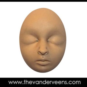 Może przedstawiać: Zbliżenie na beżową, owalną rzeźbę twarzy z zamkniętymi oczami i neutralnym wyrazem twarzy.