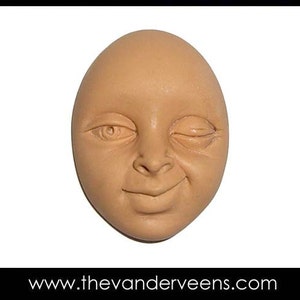 Puede incluir: Una escultura de cer&aacute;mica de una cara con un ojo cerrado y una leve sonrisa. La cara es de color marr&oacute;n claro.