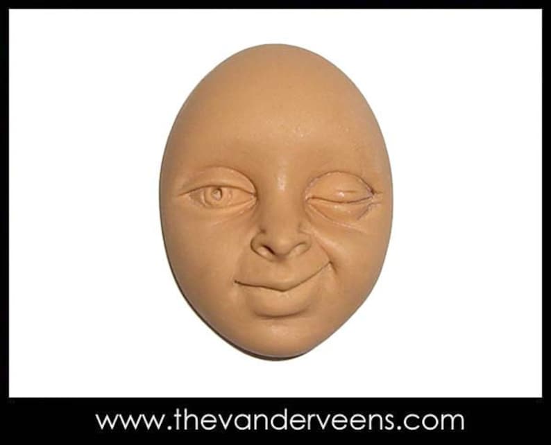 Puede incluir: Una escultura de cer&aacute;mica de una cara con un ojo cerrado y una leve sonrisa. La cara es de color marr&oacute;n claro.