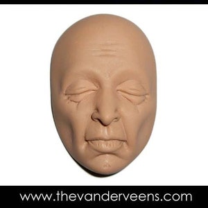 Może przedstawiać: Zbliżenie na rzeźbioną ludzką twarz w kolorze beżowym z zamkniętymi oczami. Twarz jest gładka i ma realistyczny wygląd.