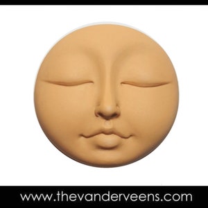 May include: A round, terracotta-colored sculpture of a face with closed eyes and a serene expression.
