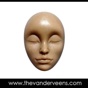 May include: A close-up of a sculpted face with closed eyes and a neutral expression. The face is made of a light brown material and has a smooth, polished finish.