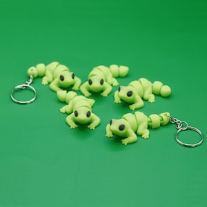 May include: Five lime green gecko keychains with black eyes. Each keychain has a silver key ring.