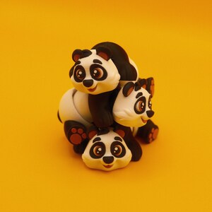 May include: Three stacked panda figurines, each with black and white fur and large, round eyes. The top panda is facing forward, the middle panda is facing to the right, and the bottom panda is facing forward. The figurines are made of a soft, pliable material.