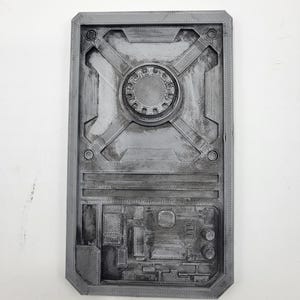 May include: A rectangular grey 3D printed panel featuring a central circular gear-like element, recessed geometric channels, and a lower section with intricate circuit board-style patterns, all finished with a weathered metallic texture.