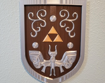 May include: A shield-shaped wall plaque featuring a brown base with a silver border. The center displays a gold-colored Triforce symbol above a silver-colored winged creature emblem, flanked by silver scrollwork and circular accents on the brown surface.