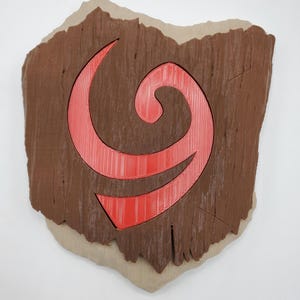 May include: A wall plaque shaped like the state of Ohio, featuring a brown textured surface that mimics wood grain. Centered on the plaque is a large, bright red, stylised swirl symbol with a layered, three-dimensional appearance.
