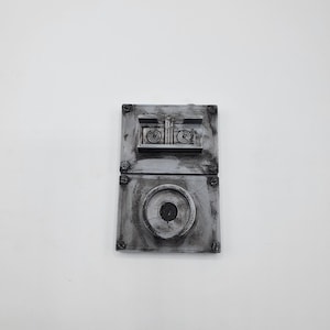 May include: A weathered, grey metal light switch with two rectangular sections. The top section has two circular elements, and the bottom section has a single, larger circular element. The switch is mounted with visible screws.