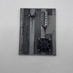 Puede incluir: Un panel rectangular gris que presenta una serie de listones verticales, un componente de ventilador negro circular y un módulo de control vertical alargado con seis botones circulares pequeños. La superficie tiene un acabado metálico.