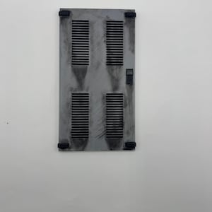 May include: A rectangular gray louvered panel featuring four distinct vertical vent sections with horizontal slats. The surface displays a weathered, distressed finish with dark smudges and black corner mounting brackets, plus a small black latch.