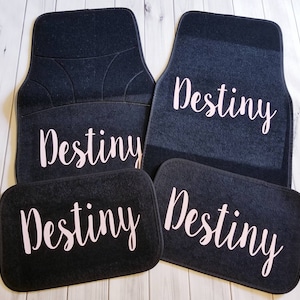 May include: Set of four black car floor mats with the name "Destiny" embroidered in pink on each mat.