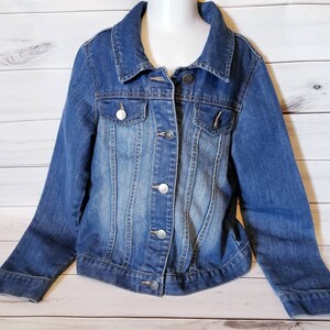 May include: A blue denim jacket with a button closure and two front pockets. The jacket has a faded look and is made of a soft, comfortable material.