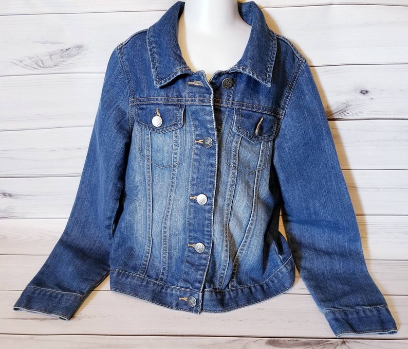 May include: A blue denim jacket with a button closure and two front pockets. The jacket has a faded look and is made of a soft, comfortable material.