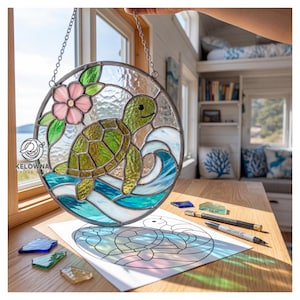 May include: A round stained glass window hanging featuring a green sea turtle swimming in blue waves, with a pink flower and green leaves. The window is held by a silver chain. The image also shows a drawing of the turtle and glass pieces.