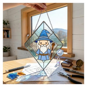 May include: A diamond-shaped stained glass panel featuring a wizard in blue robes and hat, holding a staff. The glass is clear with a textured design. The panel is suspended by a chain. The background includes a window and a wooden table.