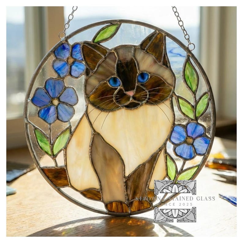 Puede incluir: Vidriera circular con un gato de ojos azules y pelaje crema y marr&oacute;n, rodeado de flores azules y hojas verdes. La obra tiene un marco met&aacute;lico y una cadena para colgar. El texto "KEPOWN STAINED GLASS SINCE 2025" est&aacute; en la esquina inferior derecha.