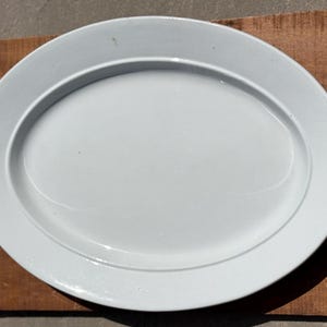 May include: A white oval serving platter with a raised rim. The platter is made of ceramic and has a smooth, glossy finish.