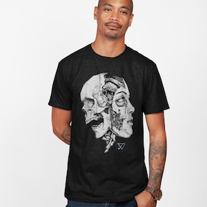 Puede incluir: Una camiseta negra con un gráfico blanco de una calavera y una cara con partes mecánicas. El gráfico está centrado en la camiseta. La camiseta la lleva puesta una persona de tez oscura.