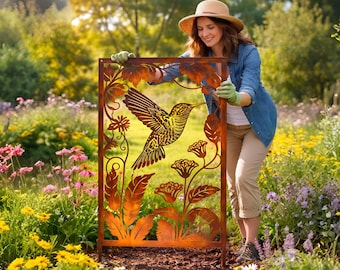 May include: A decorative metal garden screen featuring a hummingbird design. The screen is made of rusty-colored metal and has a rectangular frame. The hummingbird is depicted in flight with detailed wing and feather patterns, surrounded by floral and leaf motifs.
