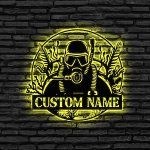 Könnte beinhalten: Ein gelber Kreis mit einer schwarzen Silhouette eines Tauchers, der eine Tauchermaske und ein Atemgerät trägt. Der Taucher ist von Seegras und Korallen umgeben. Der Text "CUSTOM NAME" ist auf einem schwarzen Banner unter dem Kreis geschrieben.