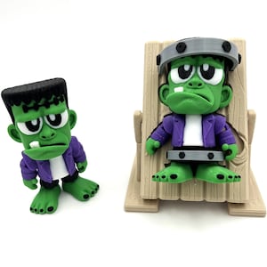 May include: Two green Frankenstein monster figurines. One stands, the other sits in a wooden chair. Both wear purple jackets and have black hair. The seated figure has a gray headpiece and a black restraint around its waist.