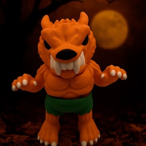 Puede incluir: Figura de monstruo naranja con dientes afilados, ojos negros y pantalones cortos verdes. La figura tiene una constitución musculosa y detalles blancos en manos y pies. Una luna llena y una silueta de árbol en el fondo.
