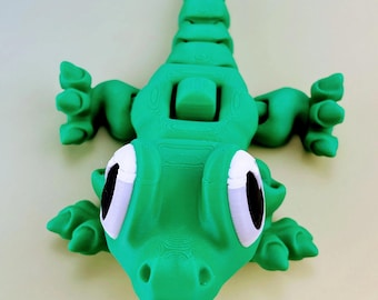 May include: A vibrant green articulated alligator toy with white and black eyes, and a segmented body. The toy has a detailed, textured surface and is posed with its legs and tail extended. The alligator is a fun, playful toy.