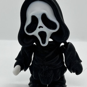 Peut inclure: Figurine imprimée en 3D du personnage Ghostface de la série de films d'horreur Scream. La figurine est principalement noire avec un masque blanc et est en position debout. L'apparence de la figurine est de type dessin animé.