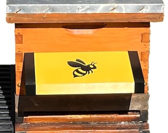 May include: A wooden beehive with a metal top. The hive is painted orange and has a yellow panel with a black bee illustration. The hive sits on a black base with a yellow and black number 8 symbol.