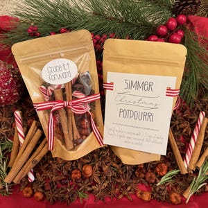 May include: Two brown paper bags filled with Christmas potpourri ingredients. One bag has a label that says "Grace It Forward" and the other bag has a label that says "Simmer Christmas Potpourri". The bags are surrounded by cinnamon sticks, star anise, and candy canes.