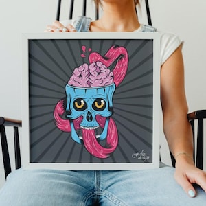 May include: A framed illustration featuring a stylized blue skull with exposed pink brain and a long, pink tongue. The artwork has yellow eyes and is set against a gray background with radial lines. The artist's signature is visible.