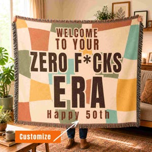Może przedstawiać: Tkany koc z wielokolorowym wzorem w kratę w odcieniach pomarańczu, żółci i turkusu. Napis "WELCOME TO YOUR ZERO F*CKS ERA" oraz "Happy 50th" wykonano dużymi, ciemnobrązowymi literami. Koc posiada wykończenie z frędzlami na krawędziach.