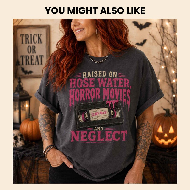 K&ouml;nnte beinhalten: Ein anthrazitfarbenes Kurzarm-T-Shirt mit einer Grafik einer schwarzen VHS-Kassette und tropfendem rosa Text, der lautet: RAISED ON HOSE WATER, HORROR MOVIES AND NEGLECT. Das Etikett in der Mitte der Kassette tr&auml;gt den Text SCARY MOVIE.