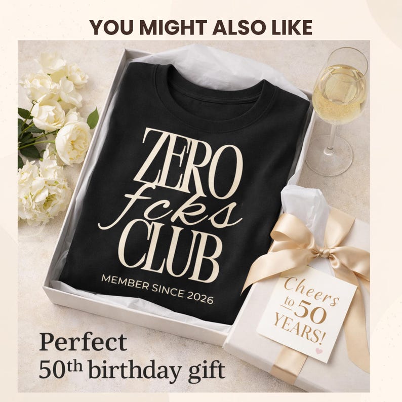 K&ouml;nnte beinhalten: Ein schwarzes T-Shirt mit Rundhalsausschnitt und dem cremefarbenen Text ZERO fcks CLUB sowie MEMBER SINCE 2026. Das T-Shirt liegt gefaltet in einer wei&szlig;en Geschenkbox neben einem Geschenkanh&auml;nger mit der Aufschrift Cheers to 50 YEARS!.