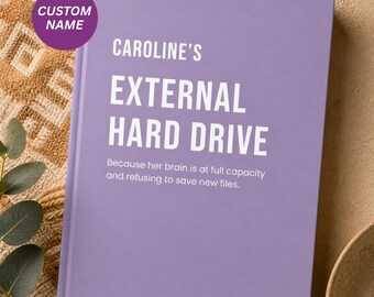 May include: A lavender-colored notebook with the text "CAROLINE'S EXTERNAL HARD DRIVE" in white. A purple circle in the upper left corner reads "CUSTOM NAME". The bottom of the notebook reads "Because her brain is at full capacity and refusing to save new files."