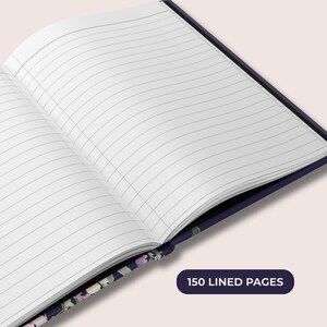 May include: Open notebook with lined pages. The notebook has a dark blue cover with floral patterns. The text "150 LINED PAGES" is displayed on a dark blue rectangular label.