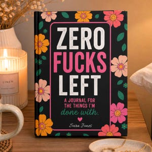 K&ouml;nnte beinhalten: Ein schwarzes Hardcover-Notizbuch mit einem Blumenmuster aus rosa, orangefarbenen und gelben Bl&uuml;ten. Das Cover zeigt den wei&szlig;en und rosa Text "ZERO FUCKS LEFT", gefolgt von "A JOURNAL FOR THE THINGS I'M done with." und dem Namen "Sara Jones".
