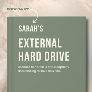Può includere: Una cover per disco rigido esterno verde salvia con la scritta bianca "SARAH'S EXTERNAL HARD DRIVE". La didascalia recita: "Perché il suo cervello è a piena capacità e si rifiuta di salvare nuovi file". La parola "PERSONALIZZA" è in alto.