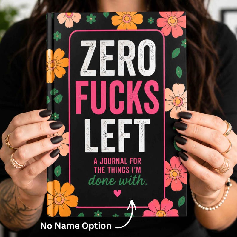 K&ouml;nnte beinhalten: Ein Hardcover-Notizbuch mit schwarzem Hintergrund und orangefarbenen, rosafarbenen und pfirsichfarbenen Blumen. Der Text lautet ZERO FUCKS LEFT, A JOURNAL FOR THE THINGS I'M done with. Ein kleines rosa Herz ist unter dem Text und ein wei&szlig;er Pfeil zeigt nach unten.