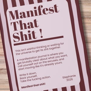 Könnte beinhalten: Ein hellrosa Notizbuch mit dem Text "Manifest That Shit!" in fetter Schrift. Das Notizbuch hat einen dunkelburgunderfarbenen Rand und enthält Text über Manifestation und Handeln.