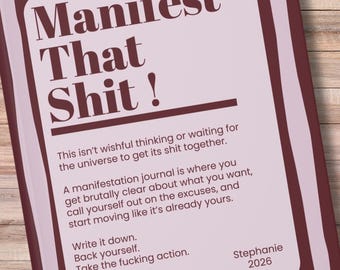 May include: A journal with the text "Manifest That Shit!" in a bold, serif font. The cover is a light pink with a dark burgundy border. The journal includes text about manifestation and taking action.