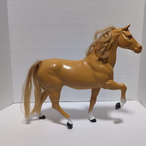 Op de afbeelding: Een bruin plastic paardenbeeldje met een vloeiende manen en staart. Het paard staat met één voorpoot omhoog, met zwarte hoeven met witte accenten. Het beeldje is ongeveer 30 cm lang.
