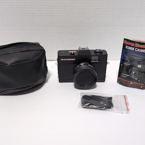 May include: A black 35mm film camera with a lens cap, a black zippered carrying case, a small black strap in a plastic bag, and an instruction manual titled Sports Illustrated 35MM CAMERA. The camera body features the text Sports Illustrated.