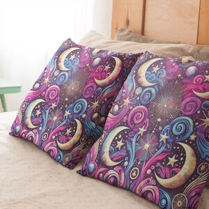 Op de afbeelding: Twee decoratieve kussens met een hemels patroon. De kussens hebben een donkerpaarse achtergrond met gouden, roze en blauwe halve manen, sterren en swirls.